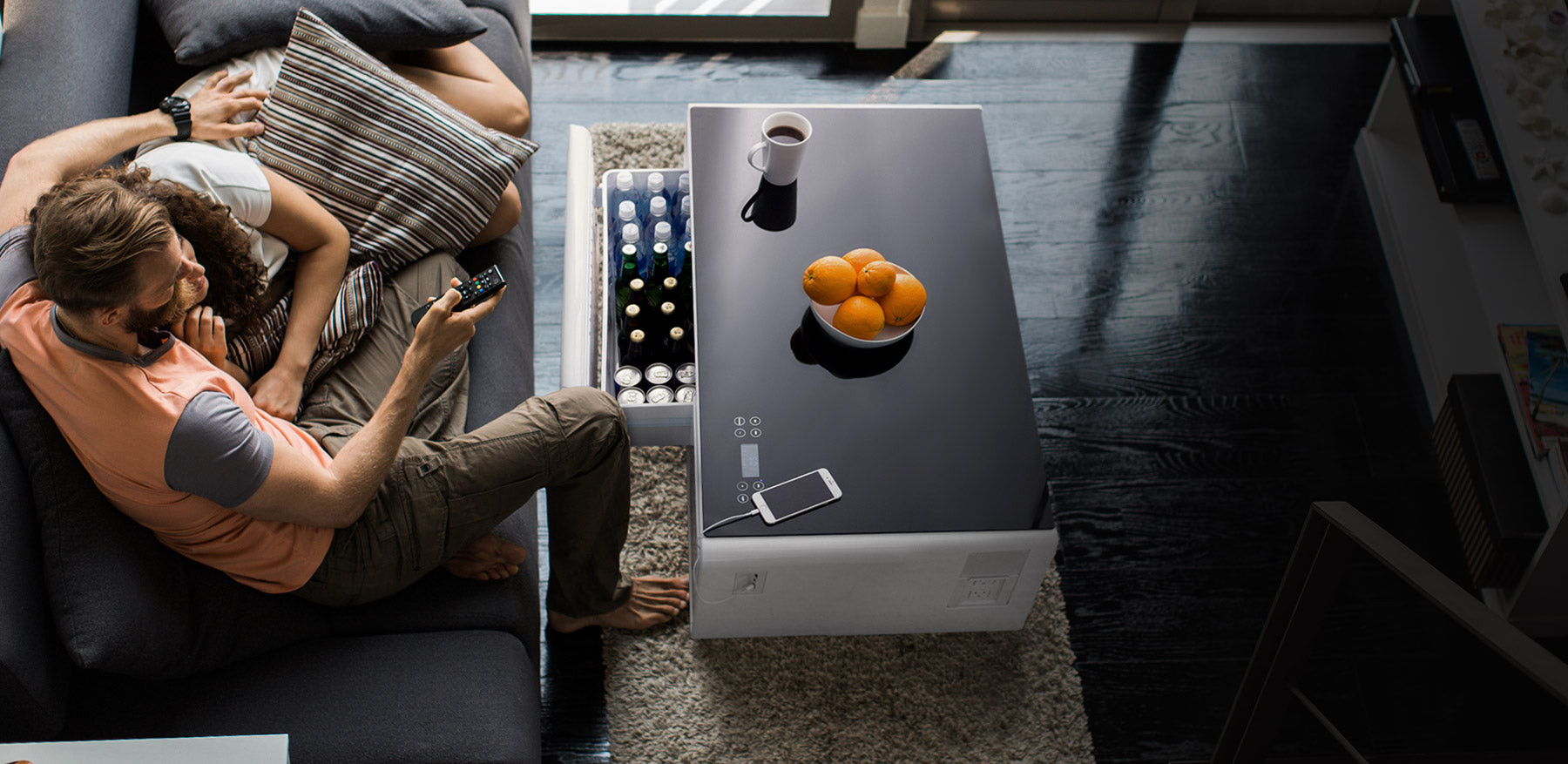 Couple watching TV in front of a Sobro Coffee Table full of drinks